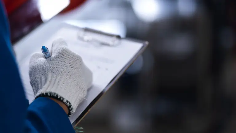 Persoon met beschermende handschoenen die een checklist of formulier op een klembord invult.