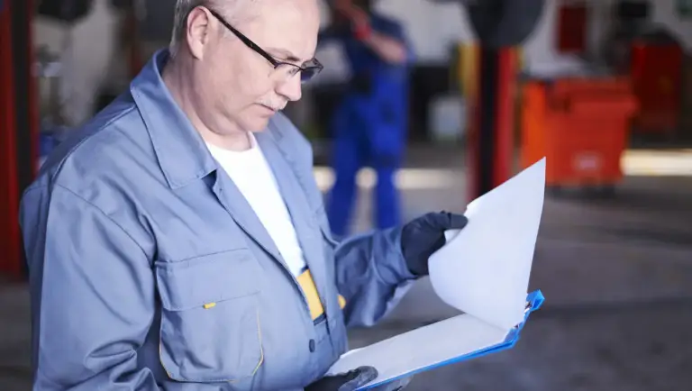 Een automonteur die in een garage werkt en een document op un klembord controleert.